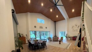 A spacious living area with a dining table, chairs, a red sofa, a ceiling fan, and large windows. - Back to nature rainforest retreat, in the centre of the Sunshine Coast Region. (Rosemount)