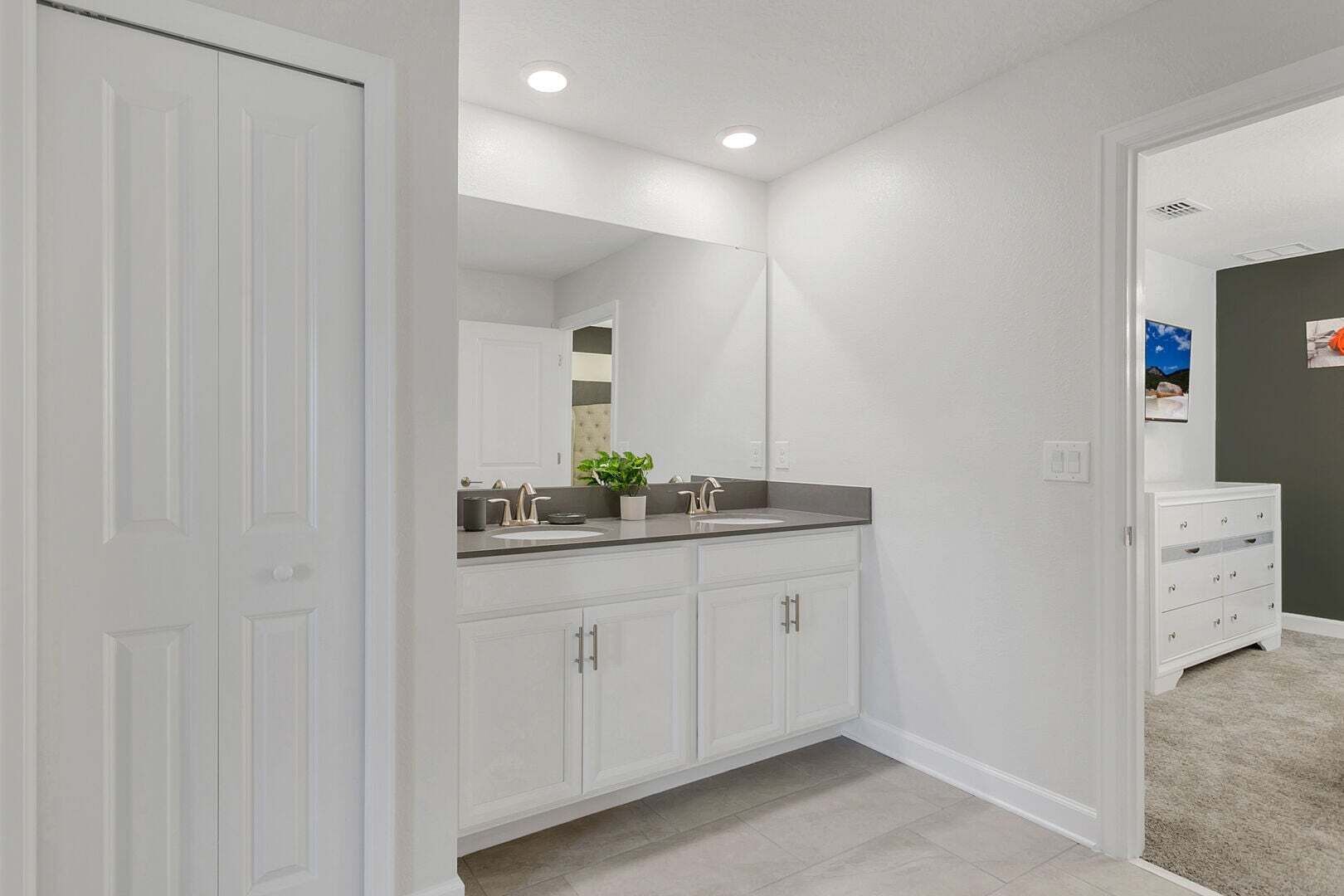 Un baño con lavamanos doble, muebles blancos, un espejo grande y una pequeña planta en maceta.