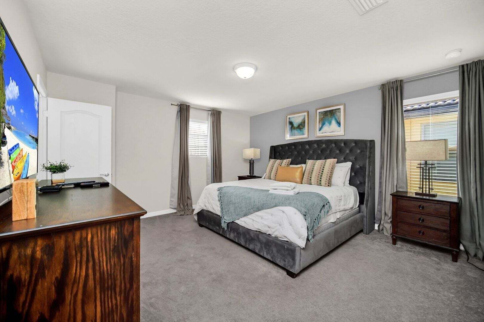 A bedroom with a large bed, a bedside table, a lamp, a dresser, and a TV on a stand.