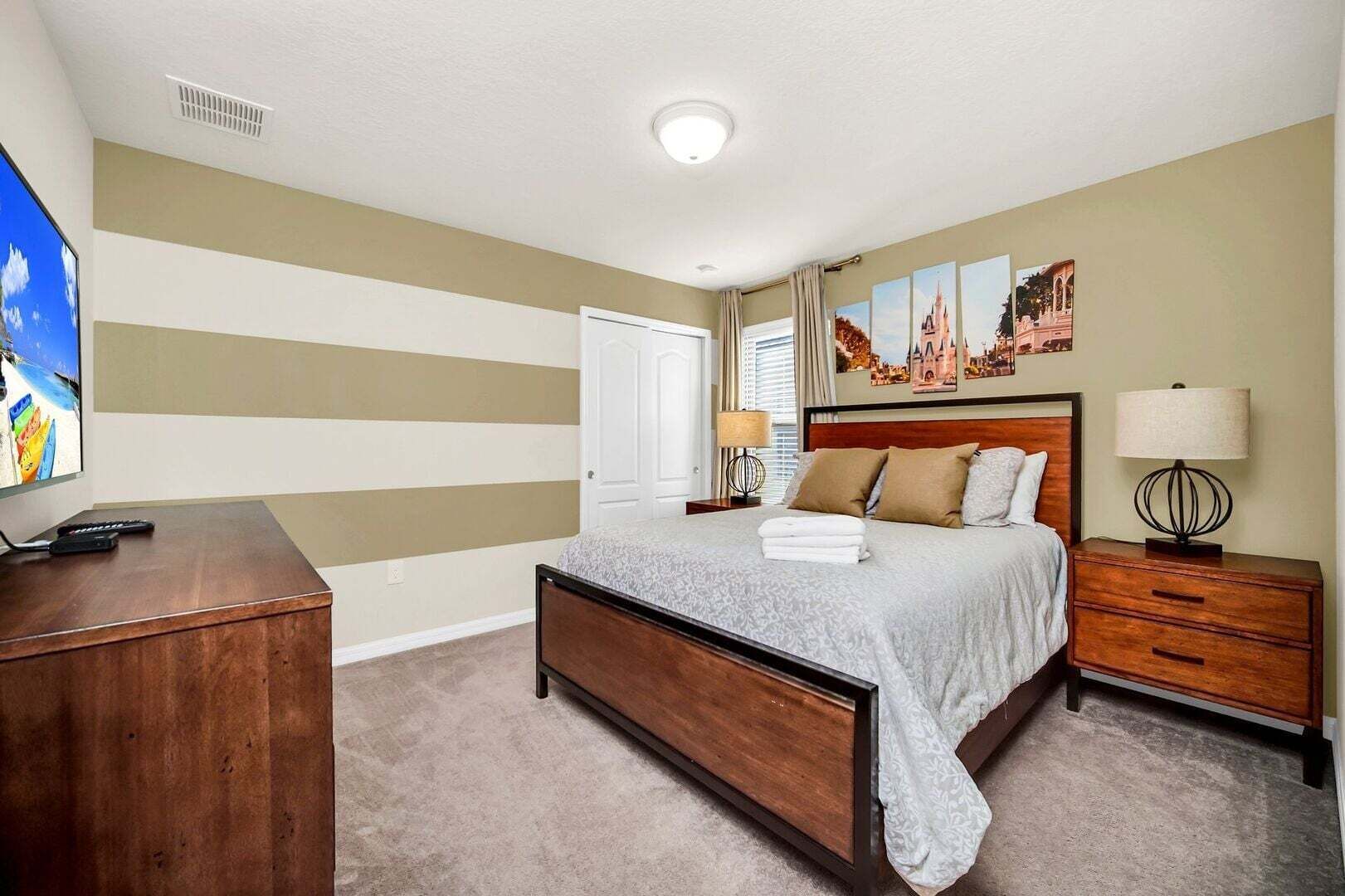 A bedroom with a bed, bedside tables, a TV, and a painting on the wall.
