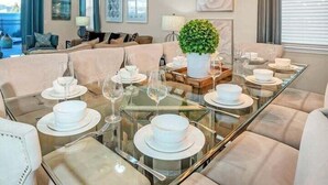 Un espace repas avec une table en verre, de l’assiette blanche et un lustre moderne.