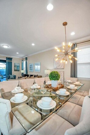 A dining area with a glass table, white plates, and a modern chandelier. - Modern Home, Private Pool. Sleeps 15 Ww102 (Kissimmee)
