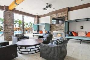 Ein Außenbereich mit Lounge-Möbeln aus Rattan, einem Kamin aus Stein und einem Pool im Hintergrund.