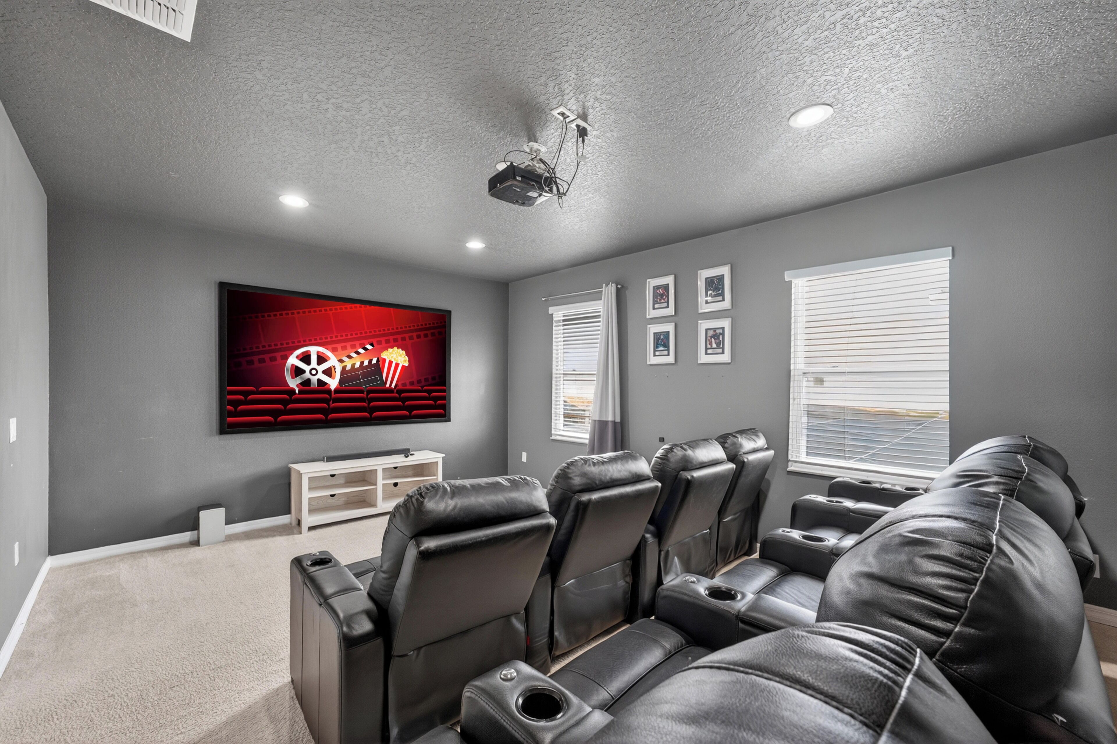 Een thuisbioscoop met een grote flatscreen-tv, luxe fauteuils van leer, een witte entertainmentkast en een projector die aan het plafond is bevestigd.