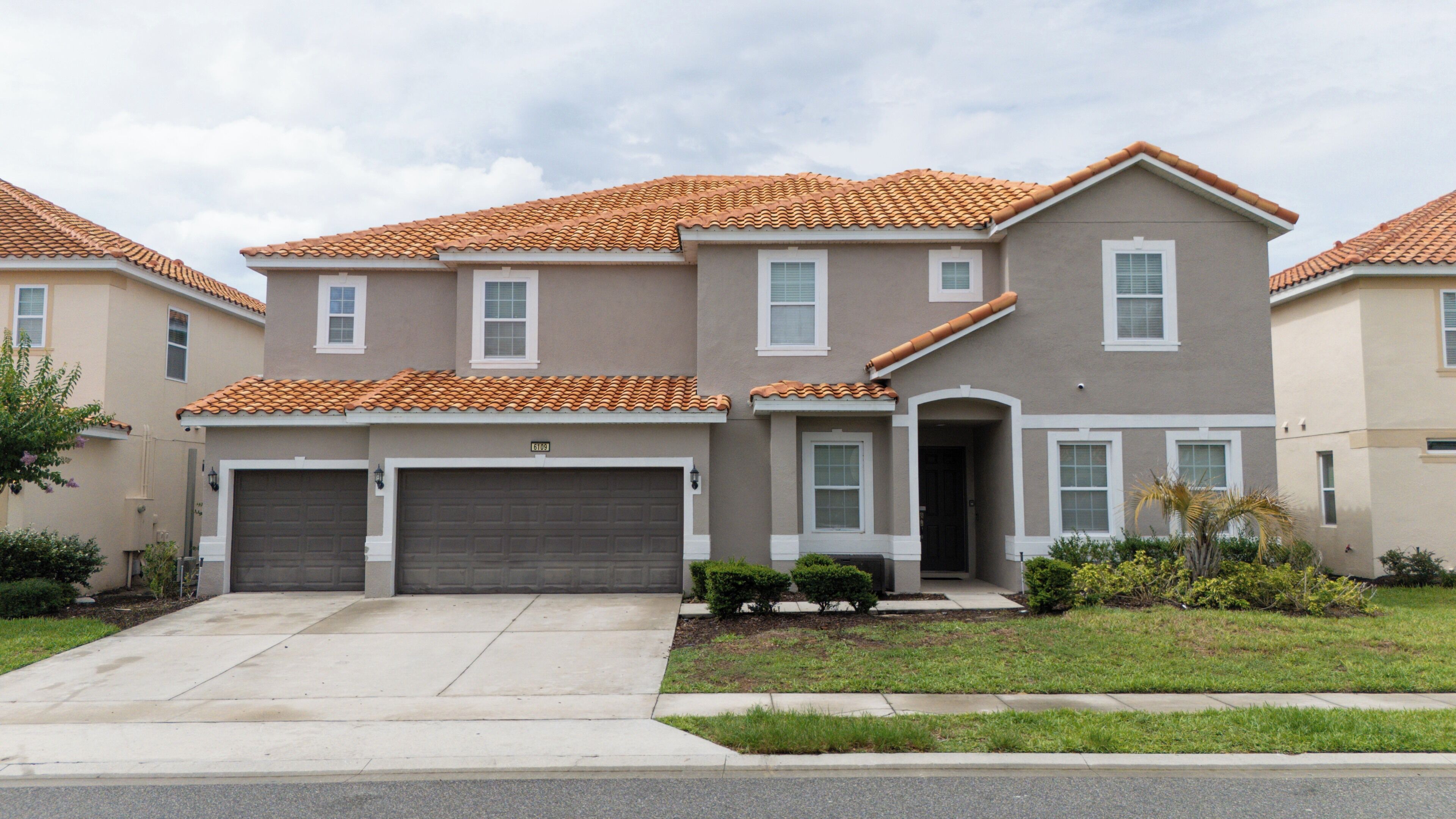 A two-story residential building with a tiled roof, a front driveway, and a small front yard.