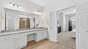 Une salle de bain moderne dotée d’un grand miroir, d’un comptoir en granit et d’une douche à l’italienne.