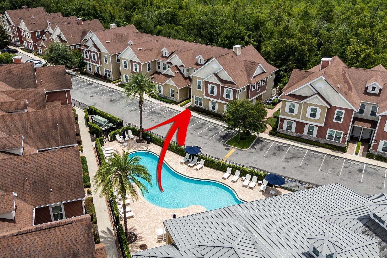 Un quartier résidentiel doté d’une piscine entourée de chaises longues et de parasols, situé à côté d’un parking.