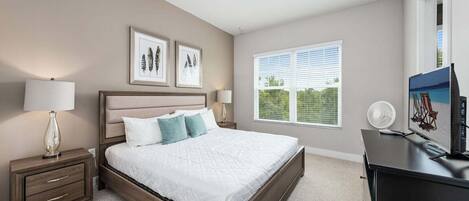 A bedroom with a bed, bedside tables, a dresser, a TV, and a window with blinds.