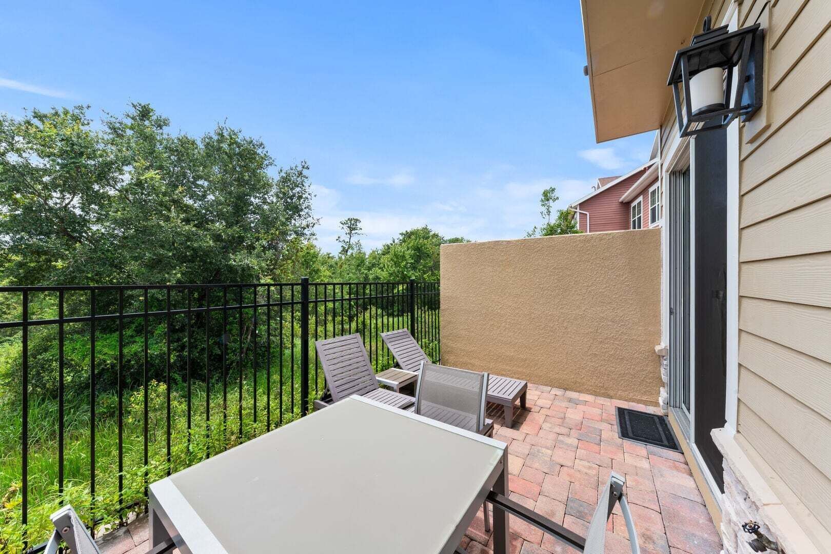 A patio with a table and chairs, a black metal fence, and a beige wall.