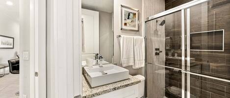Un baño moderno con cabina de ducha de vidrio, un lavamanos blanco y un inodoro.