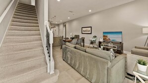 A staircase leading to a living area with a sofa, TV, and dining setup. - Ultra Convenient Stay > 5 min to Disney (Kissimmee)