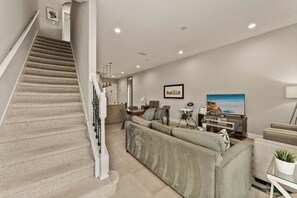 A staircase leading to a living area with a sofa, TV, and dining setup. - Ultra Convenient Stay > 5 min to Disney (Kissimmee)