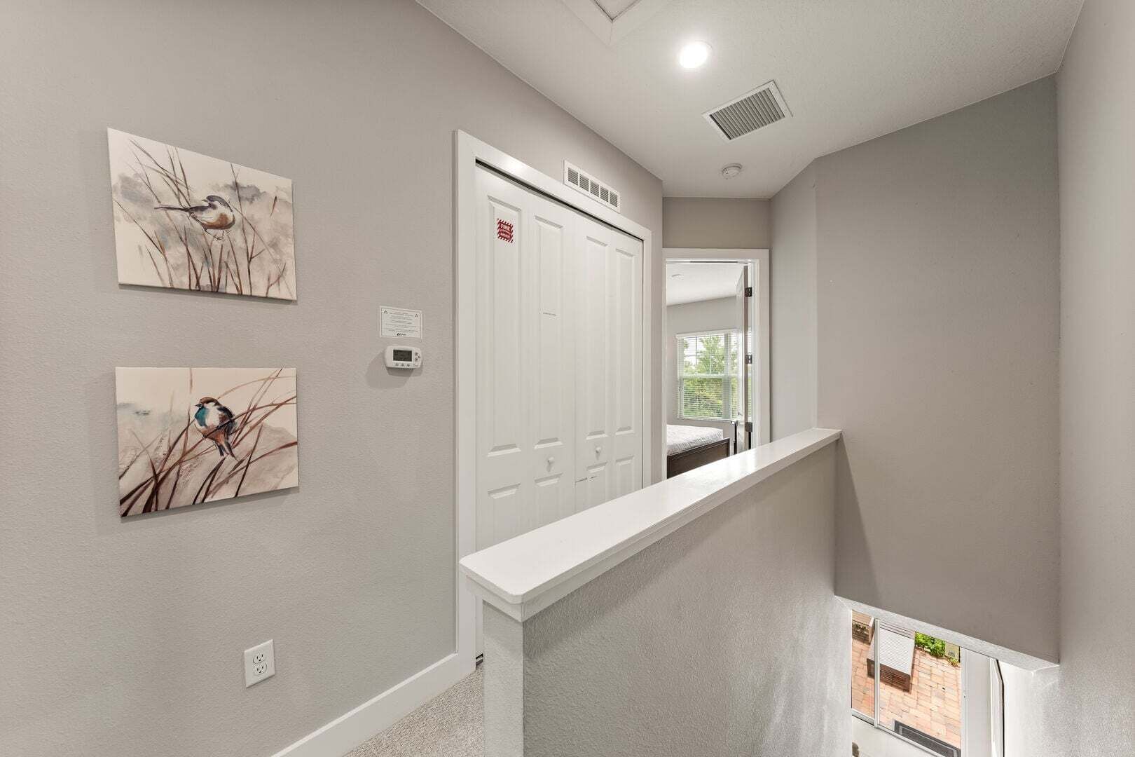 Un couloir avec une porte blanche, un thermostat et deux tableaux représentant des oiseaux accrochés au mur.