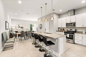 A modern kitchen with white cabinets, a central island with bar stools, stainless steel appliances, and pendant lighting. - Ultra Convenient Stay > 5 min to Disney (Kissimmee)
