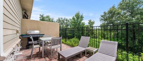 A patio with a grill, two chairs, and a table.
