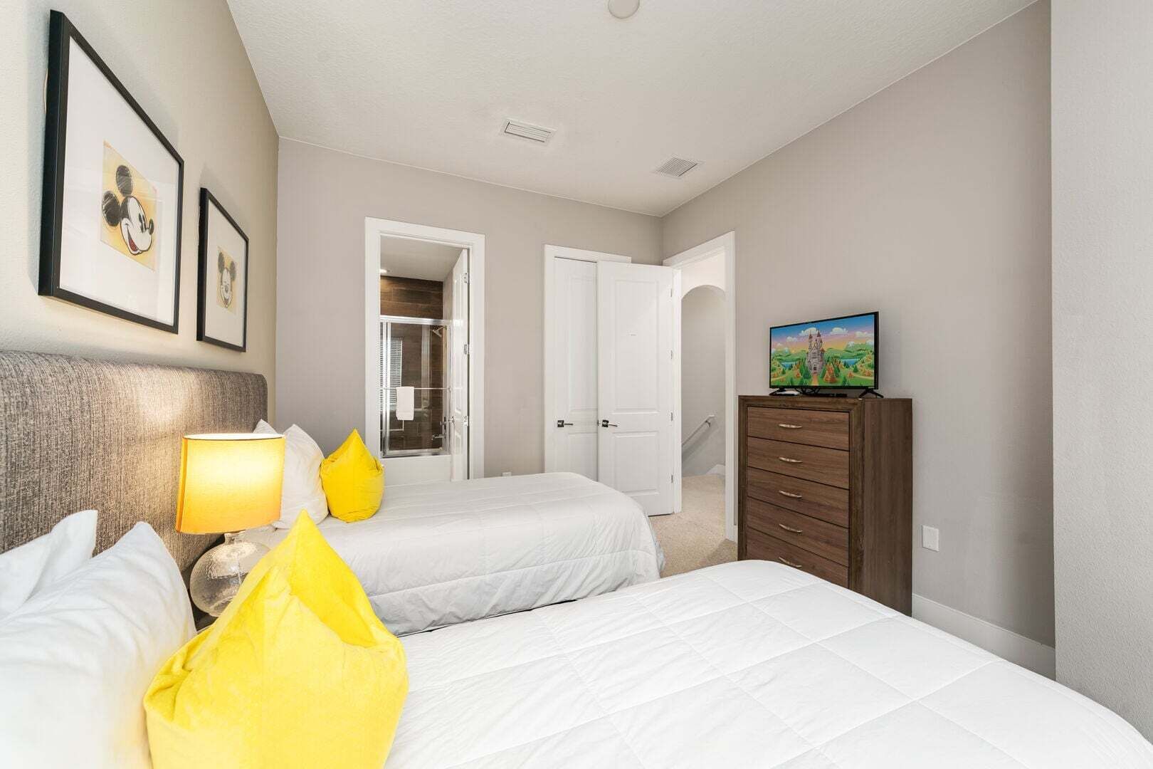 Una habitación de hotel con dos camas, televisión, cómoda y cuadros en la pared.