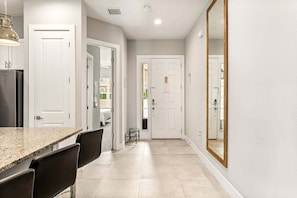 A hallway with a kitchen area, including a counter, chairs, and a refrigerator. - Ultra Convenient Stay > 5 min to Disney (Kissimmee)
