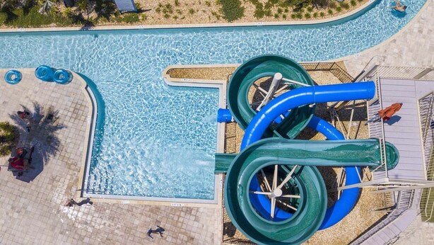 An aerial view of a swimming pool with two water slides, a tiled deck, and a few people. - Stylish Family Home Private Pool 111 (Kissimmee)