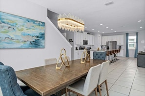 Eine moderne Küche mit weißen Schränken, ein Essbereich mit Holztisch und -stühlen sowie ein großes abstraktes Bild an der Wand.