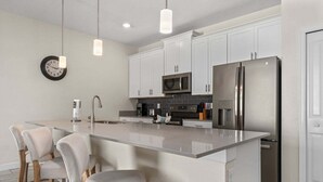 A modern kitchen with a central island, white cabinets, stainless steel appliances, and pendant lighting. - Comfy Townhome 8 Min to Disney! (Kissimmee)