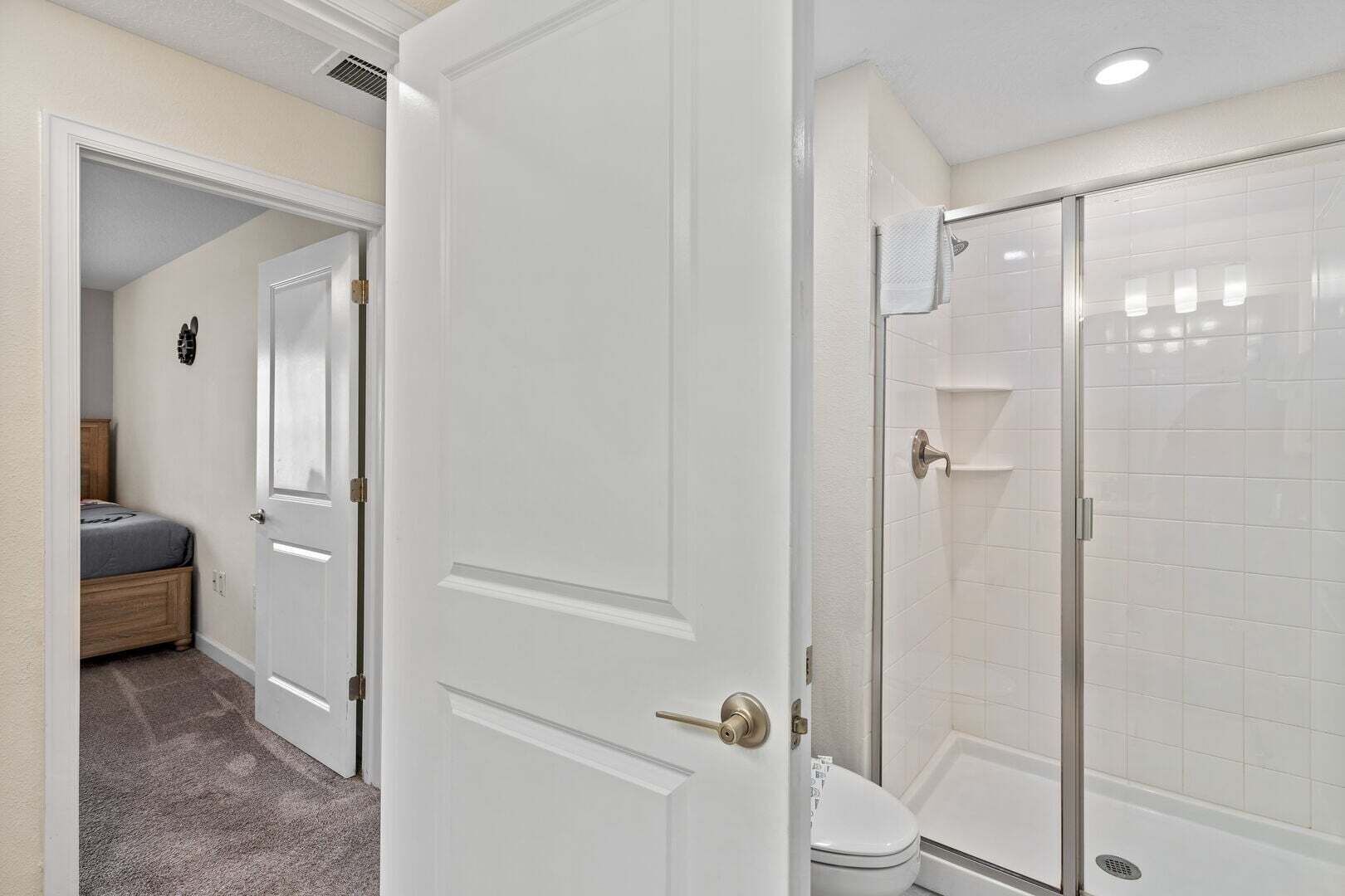 A bathroom with a shower, toilet, and a door leading to a bedroom.