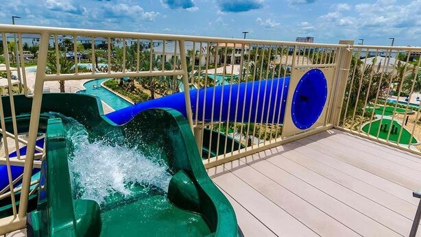 A water slide with a blue tube and a green pool at the bottom, surrounded by a wooden deck and a metal railing. - Comfy Townhome 8 Min to Disney! (Kissimmee)