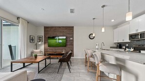 A modern living room with a TV, seating, a kitchen area, and a dining space. - Comfy Townhome 8 Min to Disney! (Kissimmee)