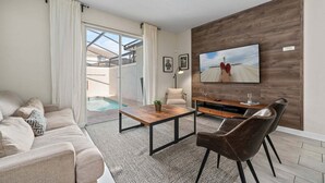 A modern living room with a sofa, coffee table, TV, and a pool view. - Comfy Townhome 8 Min to Disney! (Kissimmee)