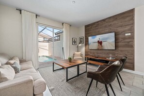 Ein modernes Wohnzimmer mit Sofa, Couchtisch, Fernseher und Blick auf einen Pool.