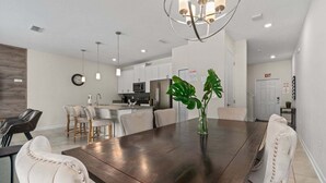A modern kitchen with white cabinets, stainless steel appliances, and a dining area with a dark wood table and upholstered chairs. - Comfy Townhome 8 Min to Disney! (Kissimmee)