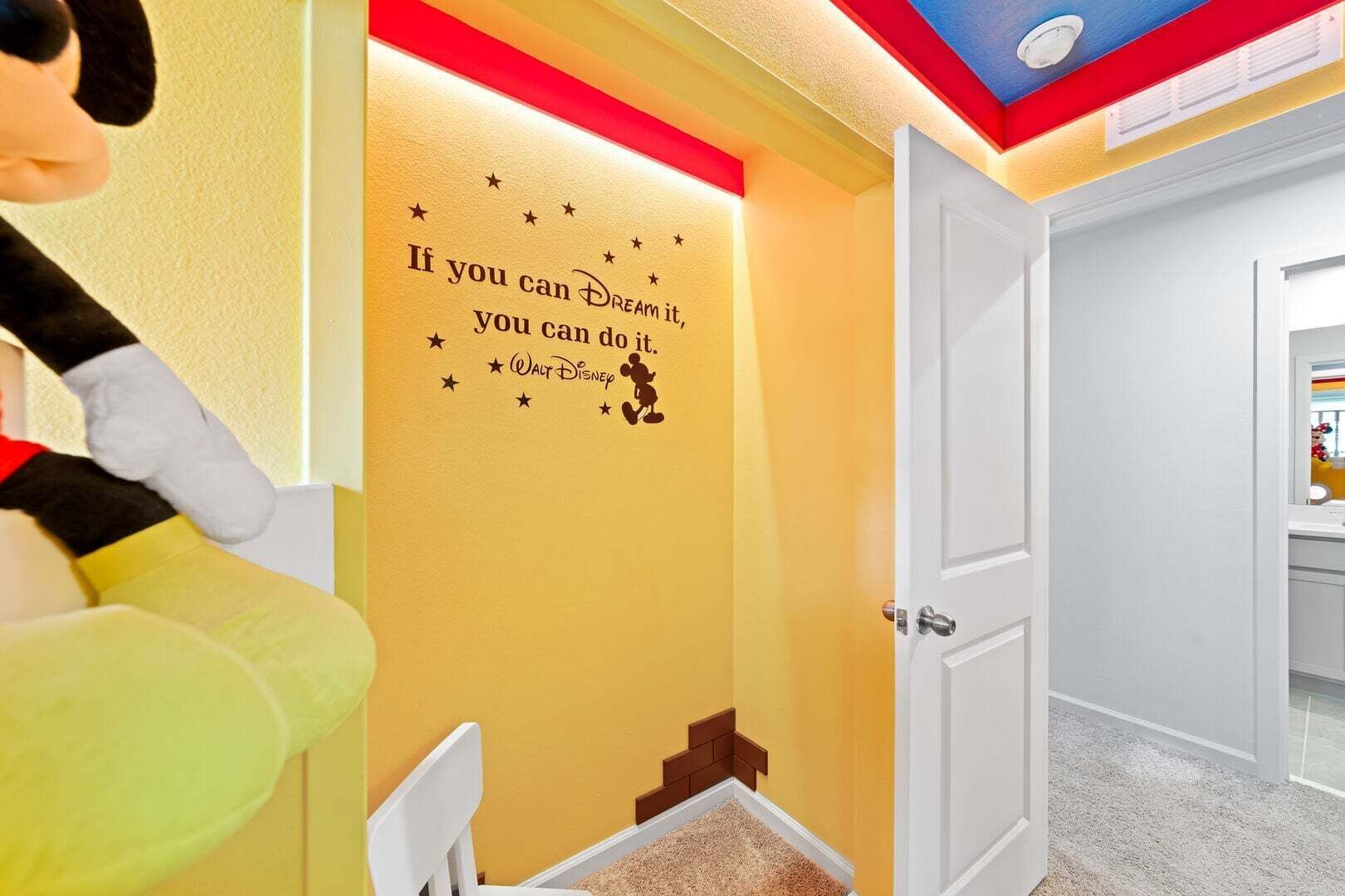 Ein Zimmer mit gelber Wand, einer Tür, einem weißen Stuhl und einer Wandsticker mit einem Zitat.