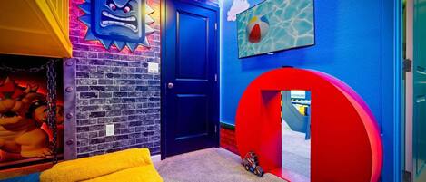 Una habitación con pared de ladrillo, puerta azul, silla amarilla y arco rojo.