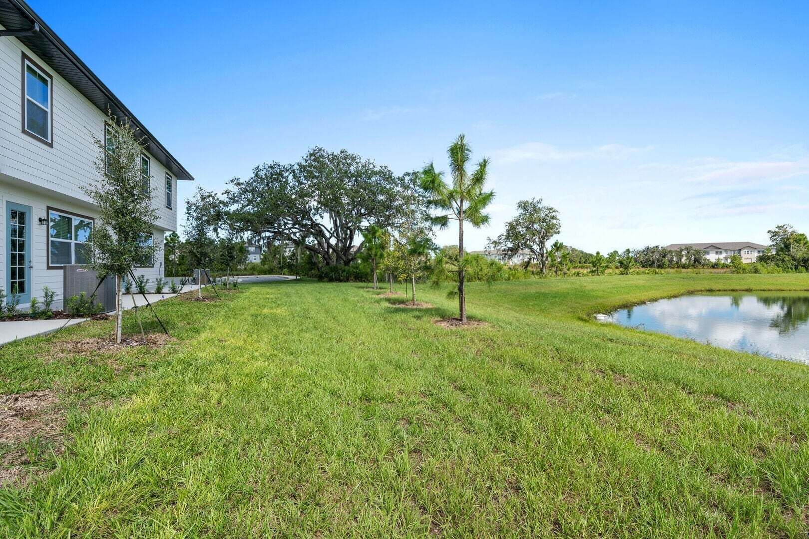 A residential area with a grassy lawn, a small pond, and a white house with a dark roof.