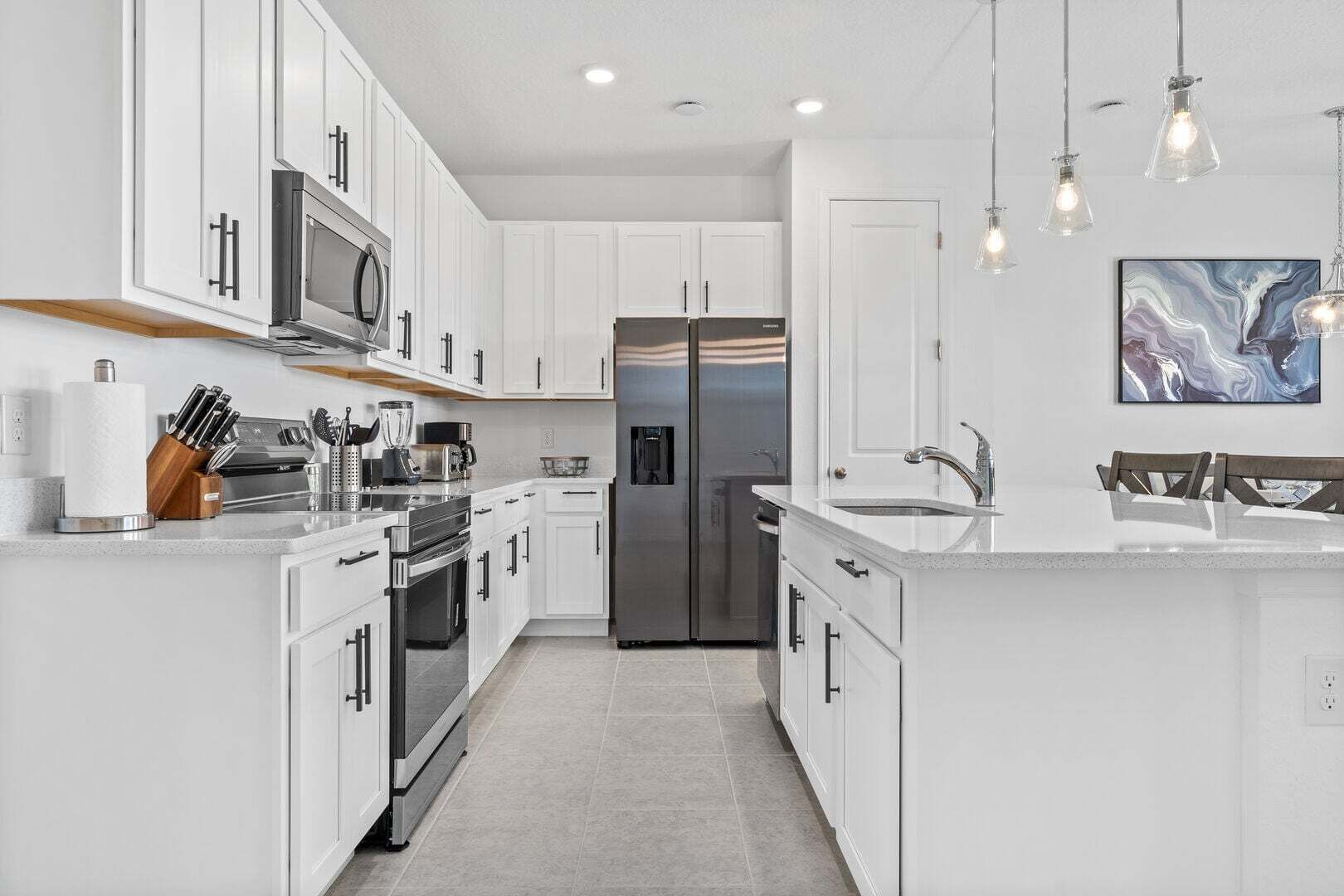 A modern kitchen with white cabinetry, stainless steel appliances, and pendant lighting.