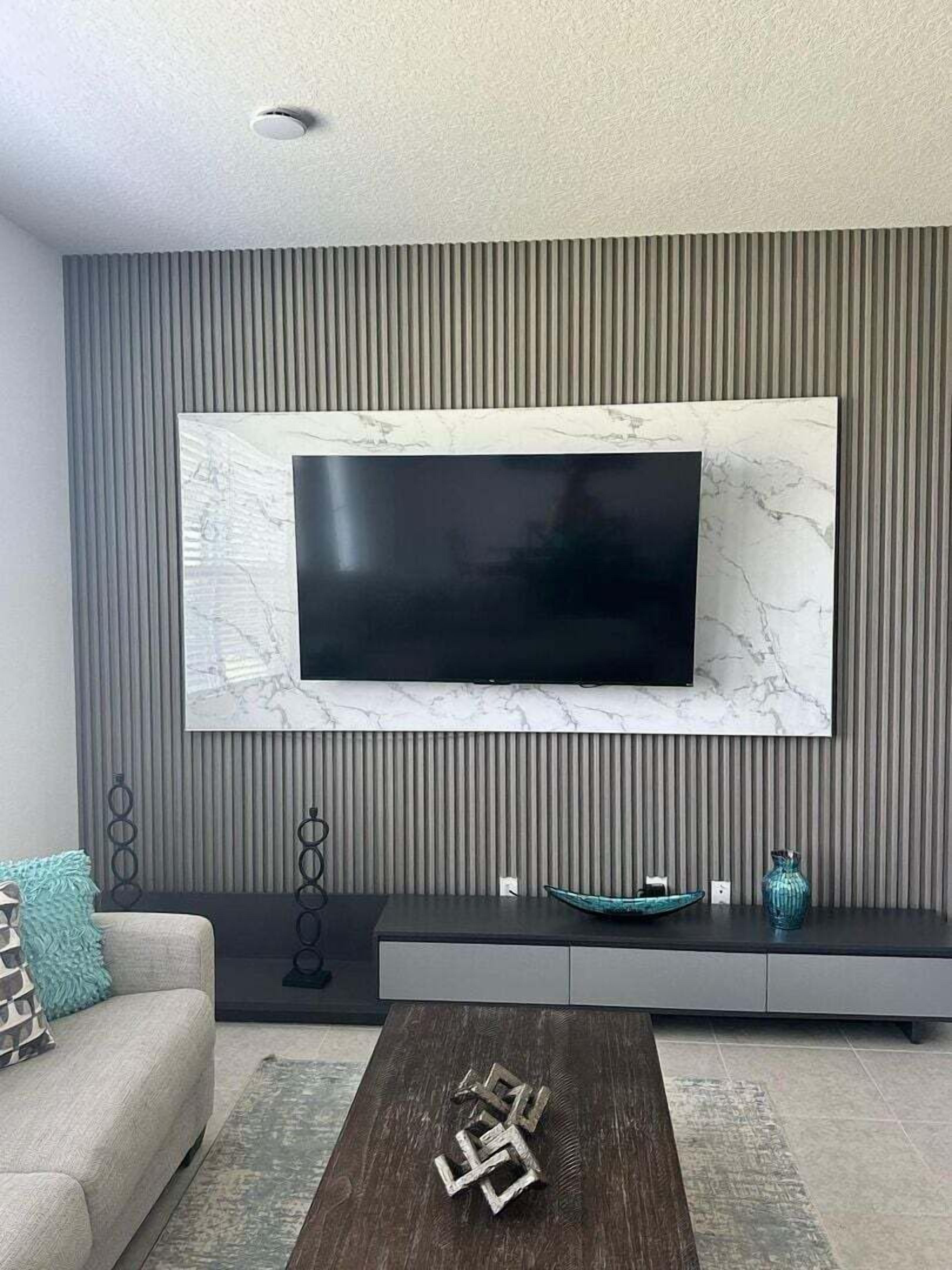 Una sala de estar moderna con un televisor de pantalla plana montado en una pared de mármol, un sofá gris, una mesa de centro oscura y una escultura decorativa de metal.