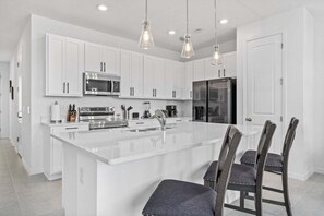 A modern kitchen with white cabinetry, stainless steel appliances, and a central island with bar stools. - Villa 3 BR, 2.5 BA Sleeps 8! (Davenport)