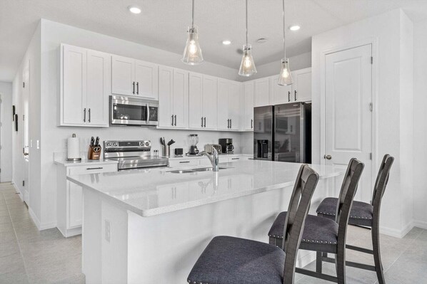 A modern kitchen with white cabinetry, stainless steel appliances, and a central island with bar stools. - Villa 3 BR, 2.5 BA Sleeps 8! (Davenport)