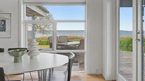 Ein Zimmer mit Esstisch, Stühlen, einer weißen Vase und Blick ins Freie durch große Fenster.