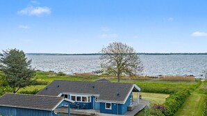 Ein blaues Haus mit Terrasse, Blick auf das Wasser und einem Baum im Hintergrund.