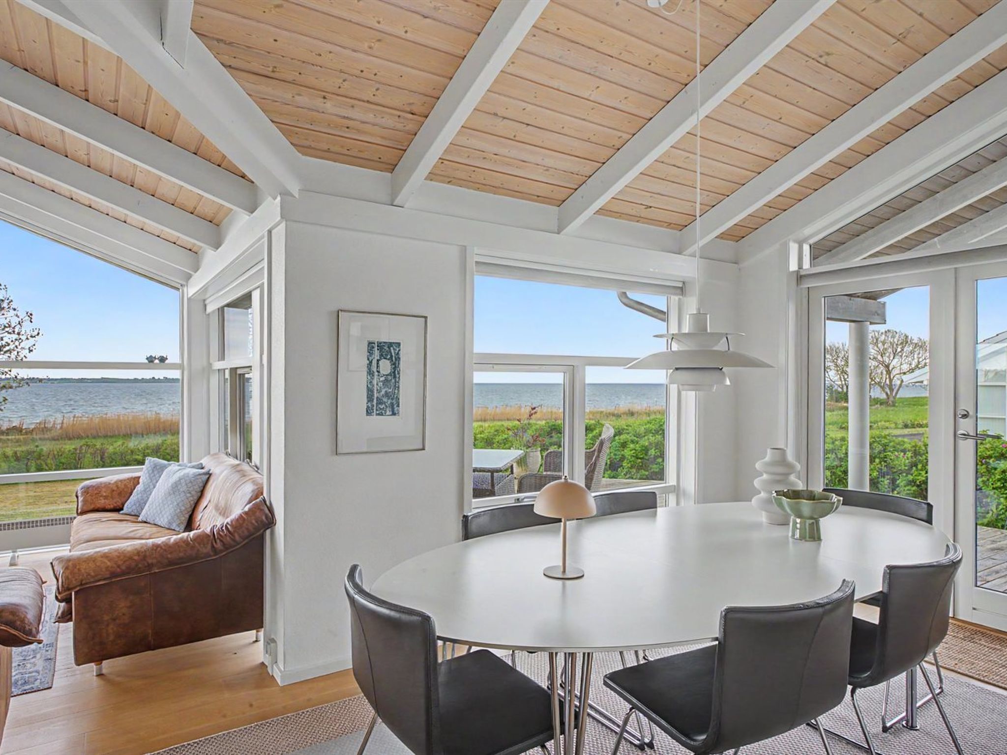 A spacious room with a large round table, a leather sofa, and a view of the sea.