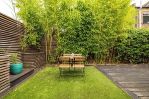 Ein kleiner Garten mit Holztisch und Bänken, umgeben von Bambus und anderer Vegetation.