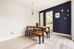 Ein Zimmer mit weißer Backsteinwand, einer dunkelblauen Akzentwand, einem Holztisch mit Bänken, einer hängenden Leuchte und einem gerahmten Bild an der Akzentwand.