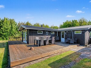 Eine Holzhütte mit Terrasse, Sitzgelegenheit im Freien und einem kleinen Fenster.