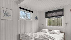 Een slaapkamer met een houten bed, twee ramen met zonwering en een lijst met een afbeelding aan de muur.