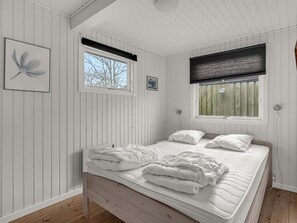 Ein Schlafzimmer mit einem hölzernen Bett, zwei Fenstern mit Jalousien und einem gerahmten Bild an der Wand.