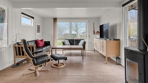 Een ruime woonkamer met houten vloer, een bank, een stoel, een tafel, een televisie en een open haard.