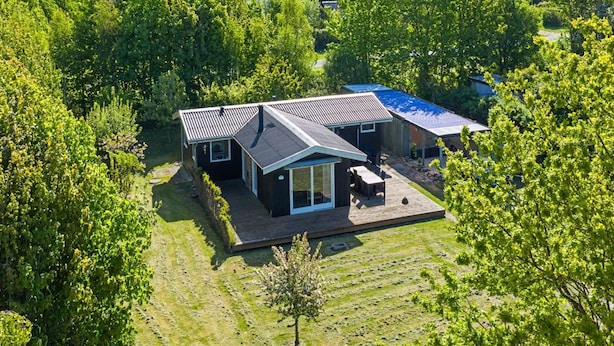 Een modern huis met een ruim terras, omringd door weelderige begroeiing en bomen.