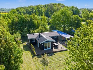 Une maison moderne dotée d’une grande terrasse, entourée d’une végétation luxuriante et d’arbres.