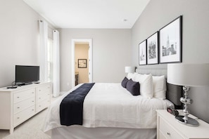 A modern hotel room with a bed, bedside tables, a TV, and framed pictures on the wall. - Gorgeous Family Villa! 114 (Kissimmee)