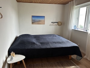 Un dormitorio con cama, una mesita, un cuadro en la pared y una ventana con cortinas.